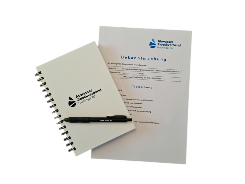 Ein Notizbuch und ein gedrucktes Dokument mit dem Titel "Bekanntmachung" sowie einem Stift sind abgebildet.