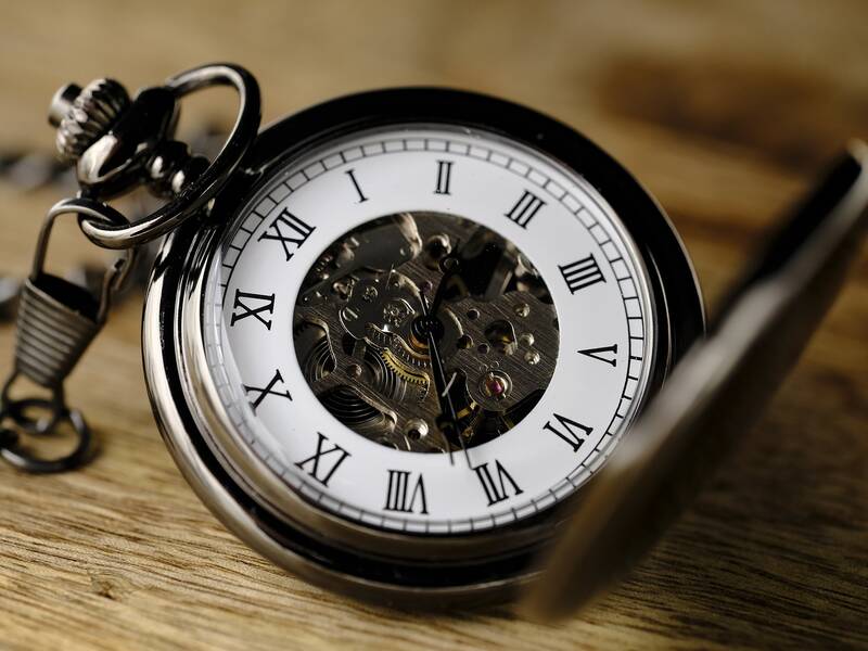 Eine geöffnete Taschenuhr mit römischen Ziffern und sichtbarem Uhrwerk liegt auf einer Holzoberfläche.