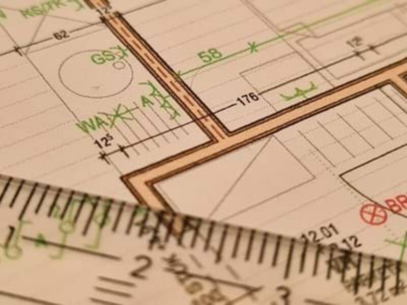 Das Bild zeigt einen technischen Bauplan mit Linealen, die auf dem Papier liegen und verschiedene Maße anzeigen.