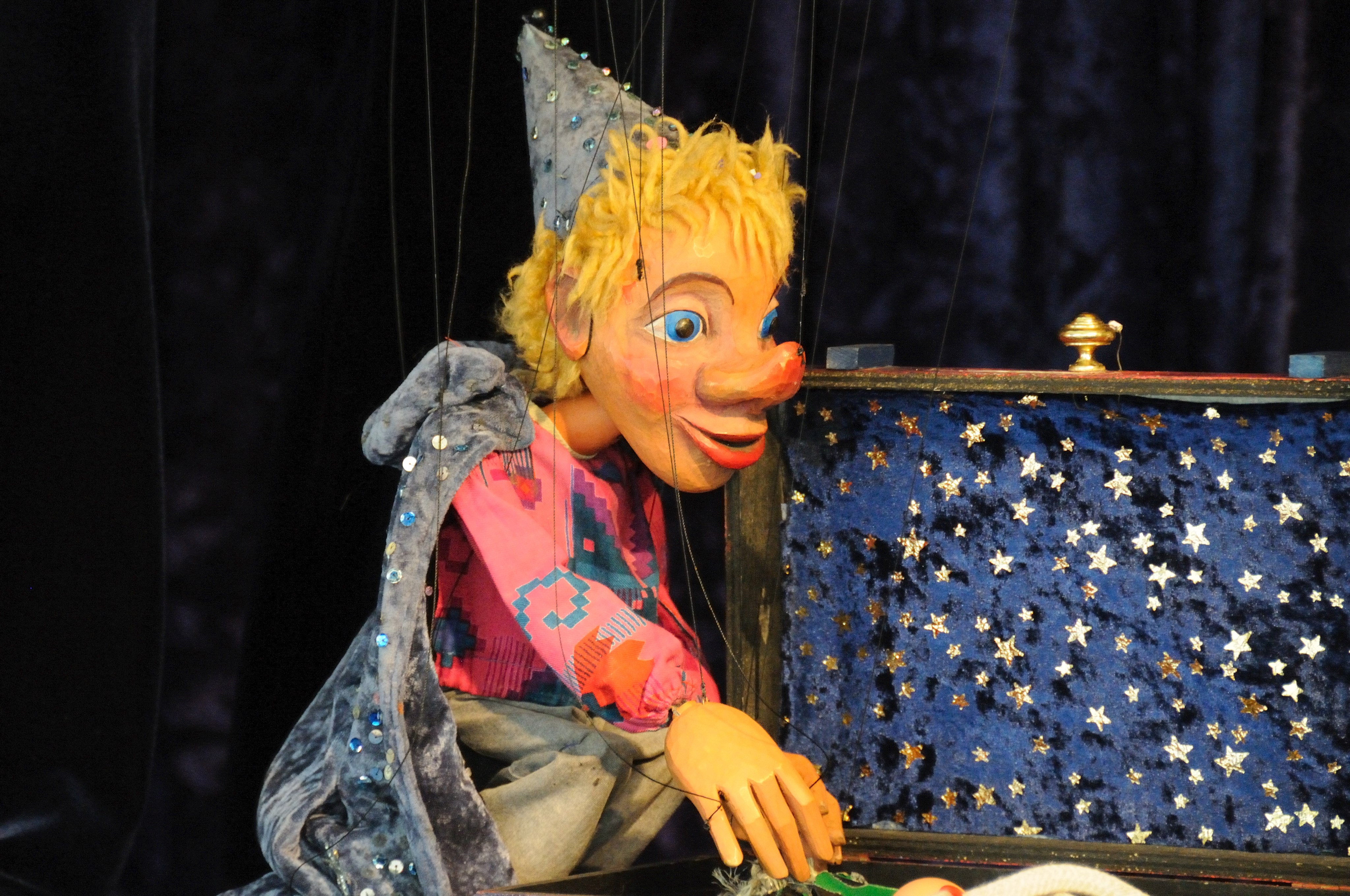 Eine Kasperl-Handpuppe sitzt neben einer Truhe