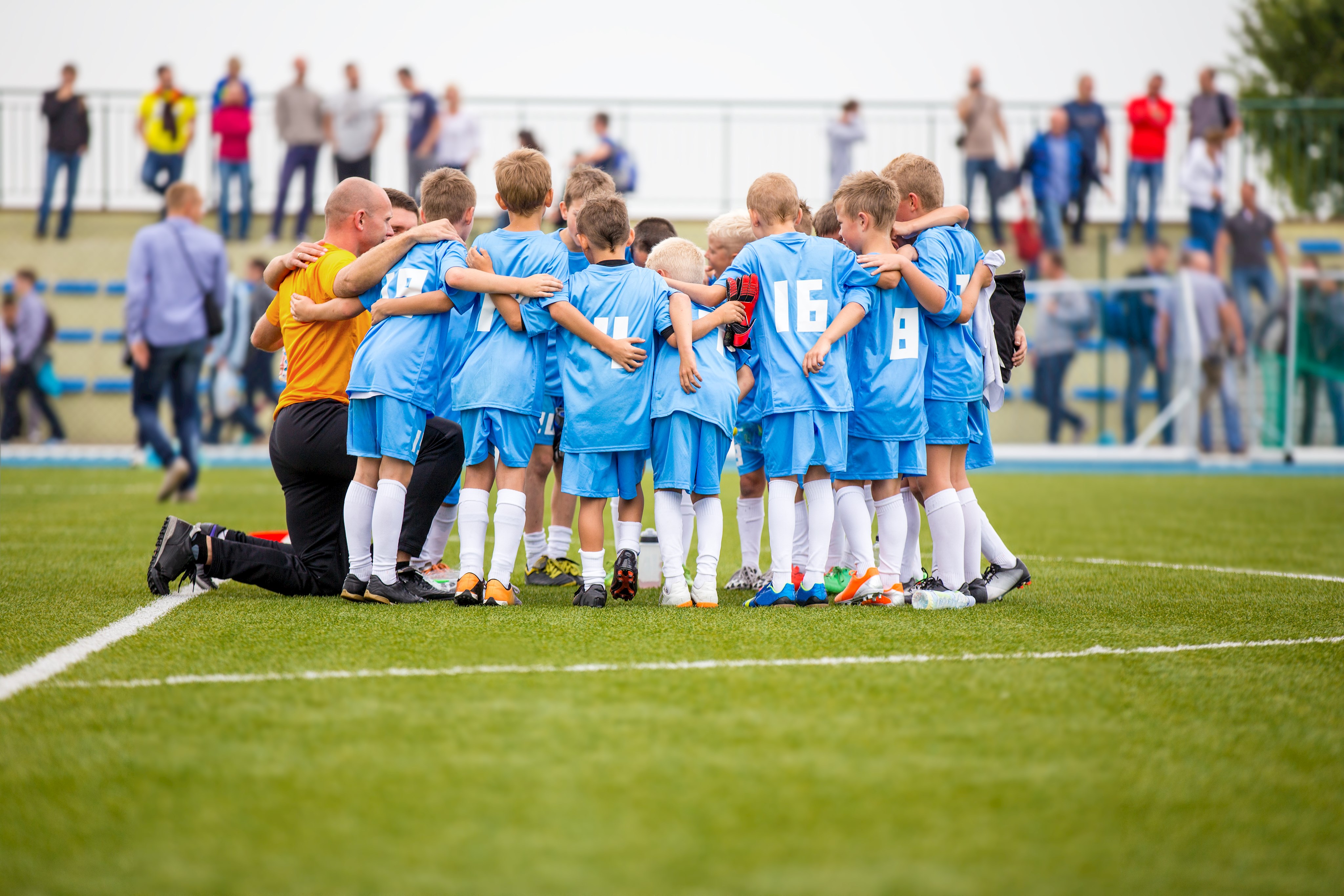 Kinder-Fussballmannschaft in Trikots bildet einen Kreis mit Trainer