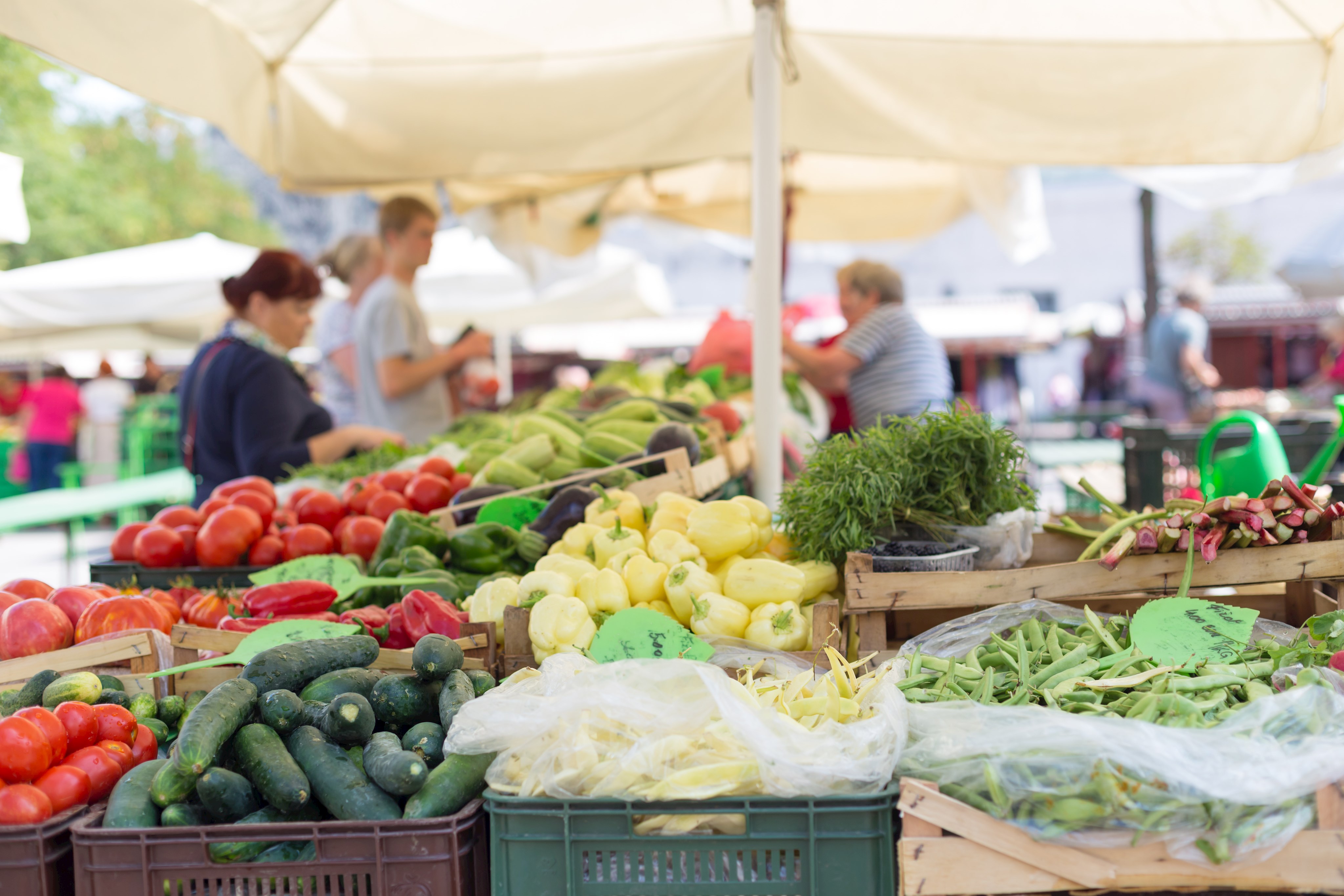 Bild eines Gemüsestands mit Marktbesuchern im Hintergrund